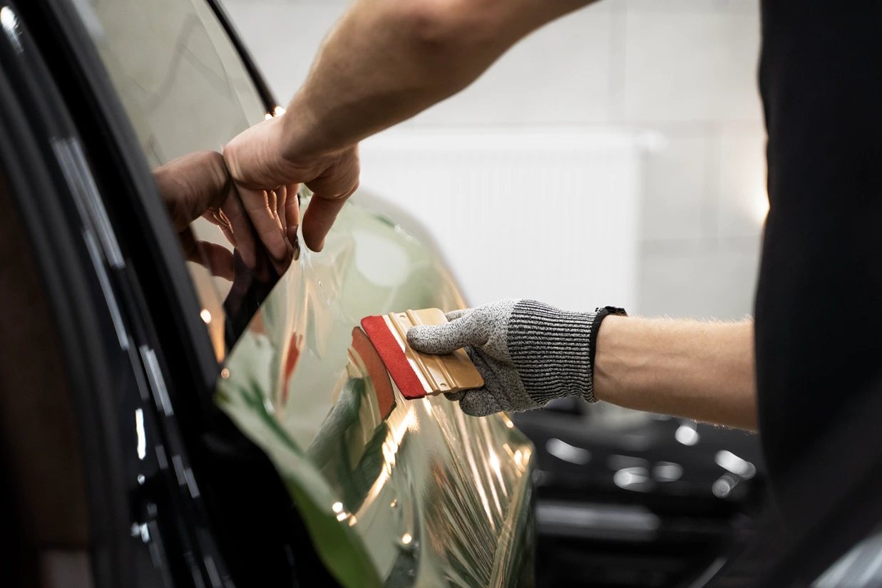 Technician applying paint protection film to car door in Brisbane workshop.