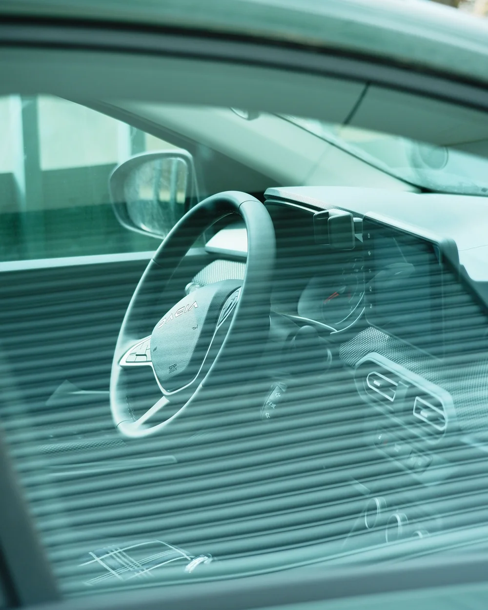 Car dashboard and steering wheel viewed through a tinted window with green-toned reflection