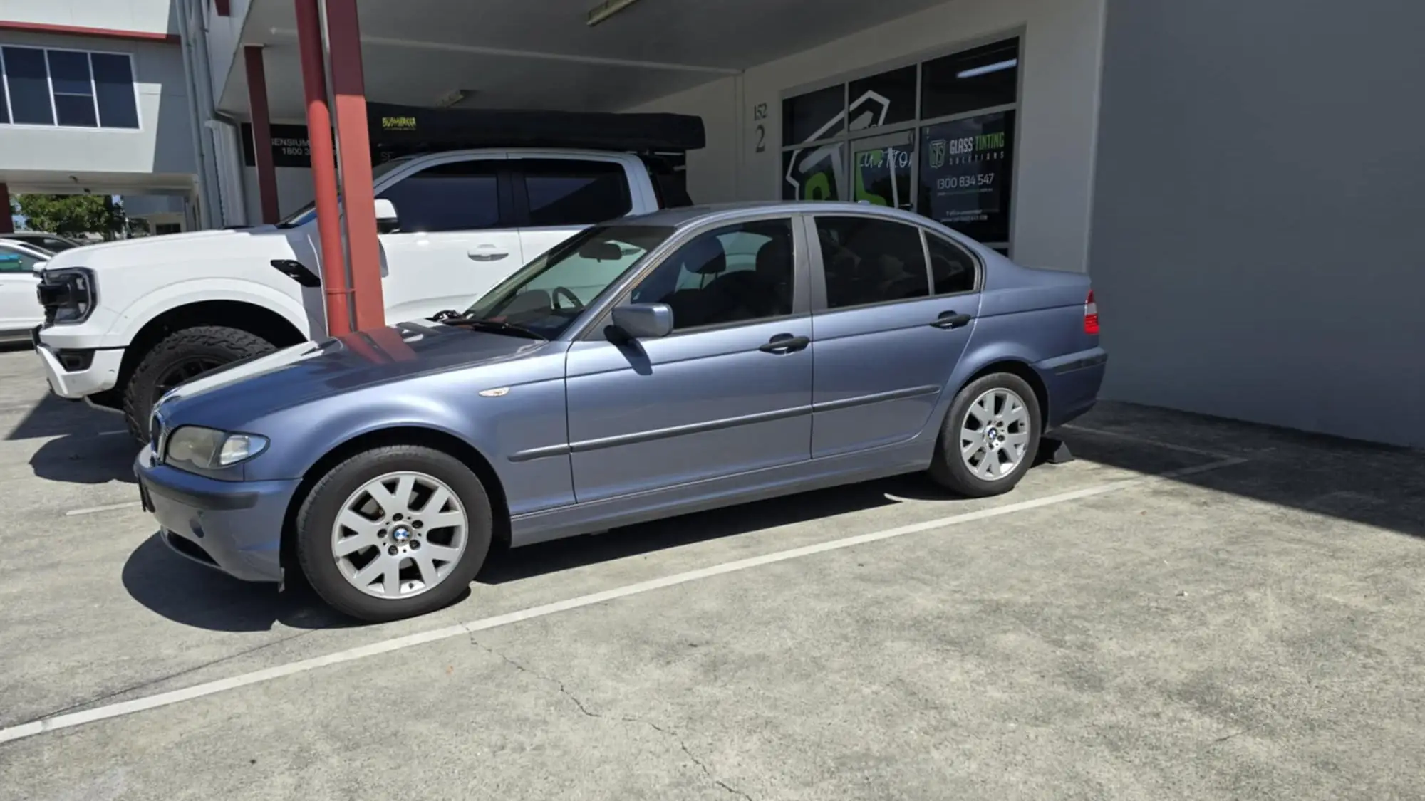 Blue BMW sedan with automotive glass tinting by GTS, parked in front of the Glass Tinting Solutions shop